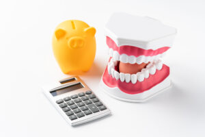 歯列矯正の治療費用のイメージ（豚の貯金箱,歯の模型,電卓）